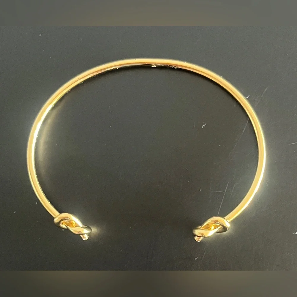 Kate Spade New York Loves Me Knot Cuff bangle in gold-tone w knot-accented ends.